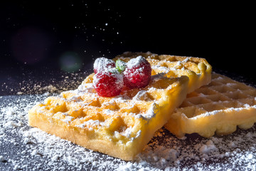Sweet toast waffles with raspberries and a sprig of mint leaves on top and sifting pouring sugar powder in the sunlight close-up macro on a black background