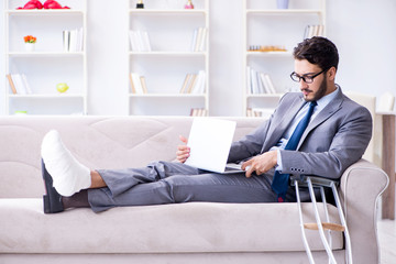 Businessman with crutches and broken leg at home working