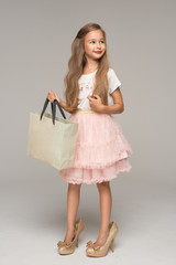 Cute little girl in pink tulle skirt and too big shoes holding packages in hand