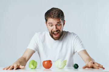 Fototapeta premium Man with a beard on a light background sits at a table, vegetables, vegetarian, diet