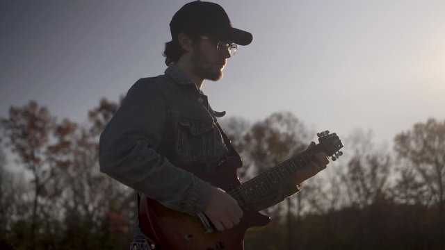 Shooting into the sun, a lone guitar player wearing a ball cap and jean jacket plays and sings.