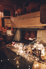 Fototapeta na wymiar Warm cozy fireplace with real wood burning in it. Magical atmosphere. Cup of hot drink and book ready for evening relax. Cozy winter concept. Christmas and travel background with space for your text.