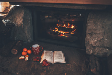 Warm cozy fireplace with real wood burning in it. Magical atmosphere. Cup of hot drink and book...