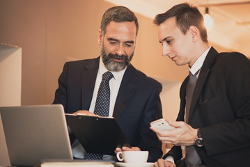 Senior business man, a boss, discussing a project with his junior employee in a coffee shop