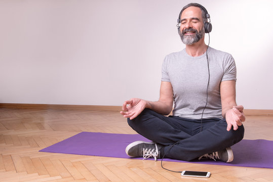 Senior Older Man Practicing Yoga And Listening To His Favourite Relaxation Music