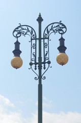 Fototapeta na wymiar Old fashioned black lamp post with patterned yellow globes, agaisnst a blue sky.