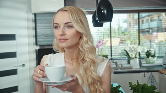 Blond charming woman drinking coffee and relaxing in her own place