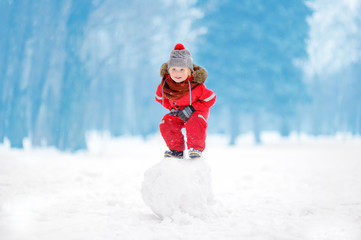 Little boy in red winter clothes having fun with snowball