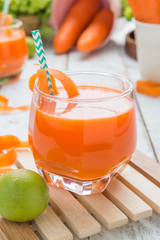 Fresh carrot juice in glass on a white wood table