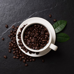 Coffee beans in the cup with leaves on the black stone.