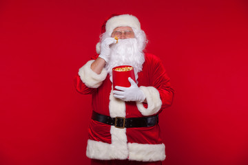 Traditional Santa Claus watching TV, eating popcorn. Christmas. Red background. emotions fear surprise