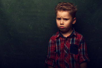 Sad confused little boy stands in dark corner