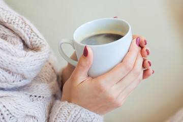 Beautiful woman holding a cup of coffee in her hands. in a knitted beige sweater