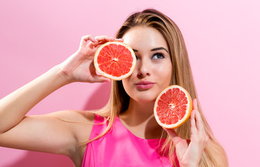 Happy young woman holding grapefruit halves on a pink background