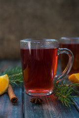 Tea in a glass mug, cinnamon stick, orange and fir branch.
