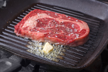 raw marble beef steak frying in black grill pan with melting butter