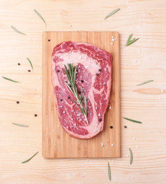 raw uncooked marble beef steak ribeye with rosemary on wooden desk, top view