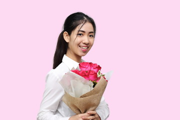 Portrait of attractive young Asian woman holding a bouquet of red roses on pink isolated background. Valentine's day concept.