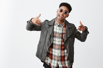 Fototapeta premium Wazzup man. Attractive young dark-skinned man with afro haircut in black leather jacket and sun-glasses laughing, gesticulating with hands, dancing and singing on party, having fun.