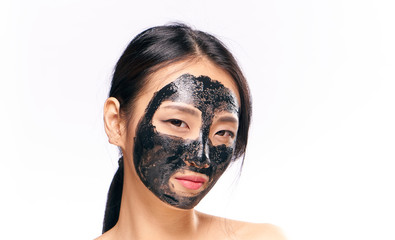 Young beautiful woman on white isolated background in black cosmetic mask for face, asian, portrait