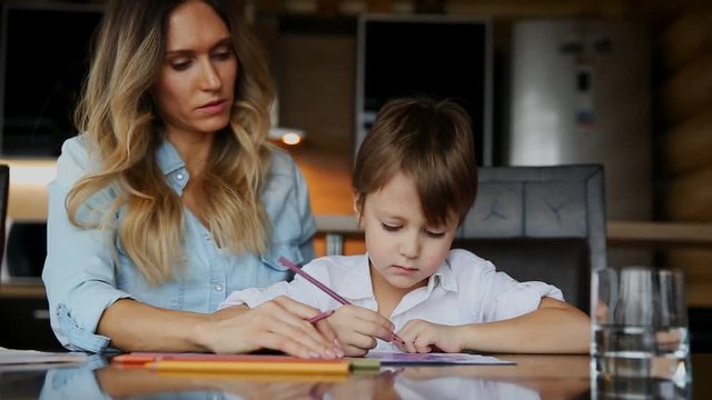 Beautiful mom helps her son to paint with colored pencils image. Helping to develop a child's imagination.