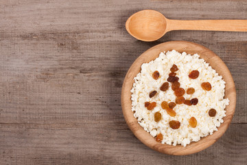 Cottage cheese with raisins in a wooden bowl on old wooden background with copy space for your text. Top view