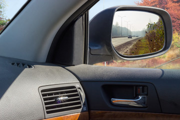 Reflected highway in car side rear-view mirror in autumn