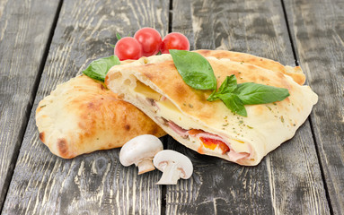 Baked calzone, raw mushrooms, cherry tomatoes on wooden surface