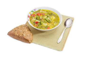 Bowl of vegetable soup, brown bread and spoon on napkin