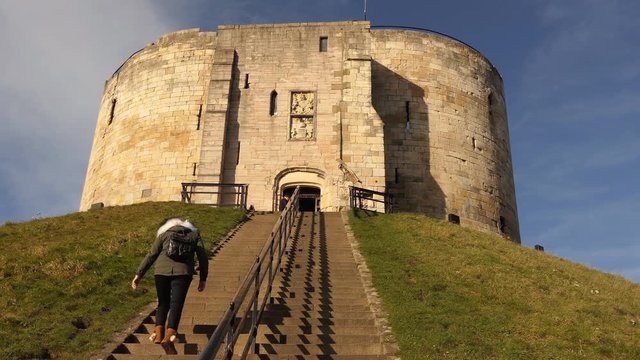 Long haired woman wearing autumn or winter coat is climbing York castle Cliffords tower stairs on a sunny day, England, United Kingdom