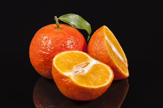 Fruits of mandarin orange ,whole and cut, on black background, reflection