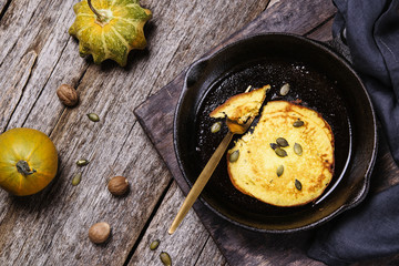 Homemade pumpkin pancakes on cast iron frying pan on vintage wooden table. Fall's breakfast. Selective focus 