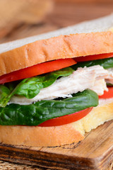 Easy chicken sandwich for lunch or dinner. Chicken sandwich with fresh red tomatoes and spinach leaves on a wooden board. Vertical photo