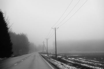 A deserted highway is in the fog in black and white