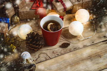 Beautiful composition. Snowfall. On a wooden background, gifts, a cup of tea, gifts, fir cones and garlands