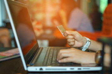 Woman using laptop to online shopping and pay by credit card. Selective focus at woman's hand and use warm bright sunlight filter for feeling comfortable