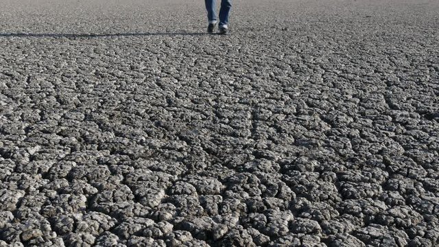 Man in jeans and boots walking on dry cracked land