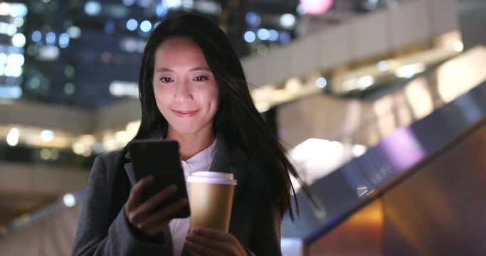 Woman use of cellphone and hold coffee cup in city at night