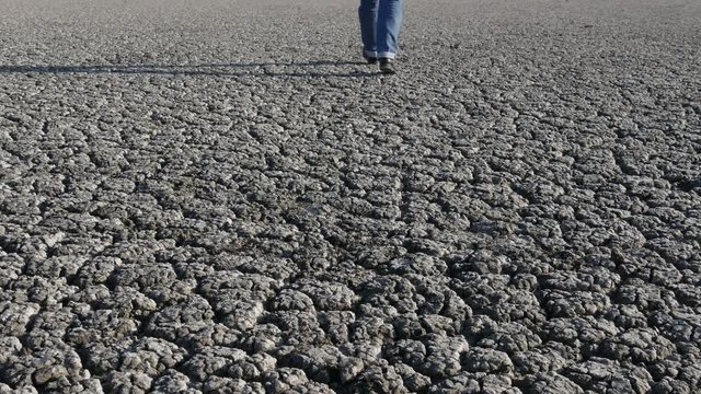 Man in jeans and boots walking on dry cracked land