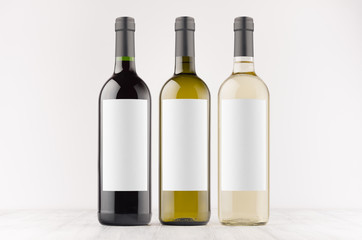Transparent, green, black wine bottles with blank white labels on white wooden board, mock up. Template for advertising, design, branding identity.