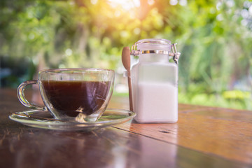 Coffee cup and sugar bottle on wooden table in garden
