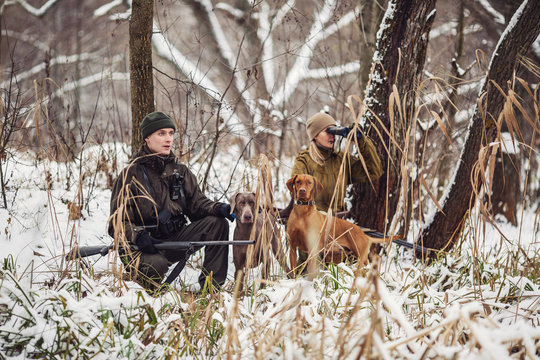 two hunters with rifles in a snowy winter forest.