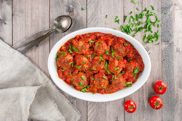 Plate with cooked meatballs with tomato sauce on the wooden table