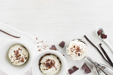 Portions of vanilla ice-cream with chocolate topping in the white plates on the wooden table, top view