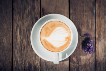Top view of hot coffee in green cup with latte art on wooden plank table with forget me not flower,Food and drink concept,vintage filter.