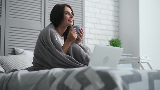 Have anice day. Delighetd bice woman sitting in bed and drinking her coffee while feeling delighted