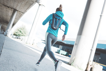 Athlete beautiful girl with water-backpack runnig in the morning on the city street. Sport tight clothes. Urban workout.