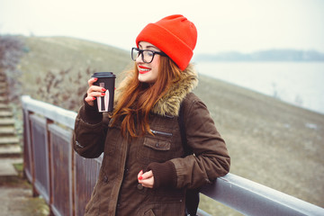 Cute funny smiling and laughing hipster girl wear coat eyeglasses in red hat and red lipstick at cold weather. Lifestyle modern young people, positive life and enjoying