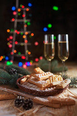 homemade cookies, glasses with champagne and a New Year tree on a festive table on a background of multi-colored New Year's lights