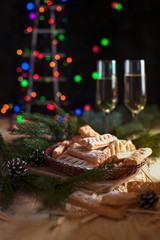 homemade cookies, glasses with champagne and a New Year tree on a festive table on a background of multi-colored New Year's lights
